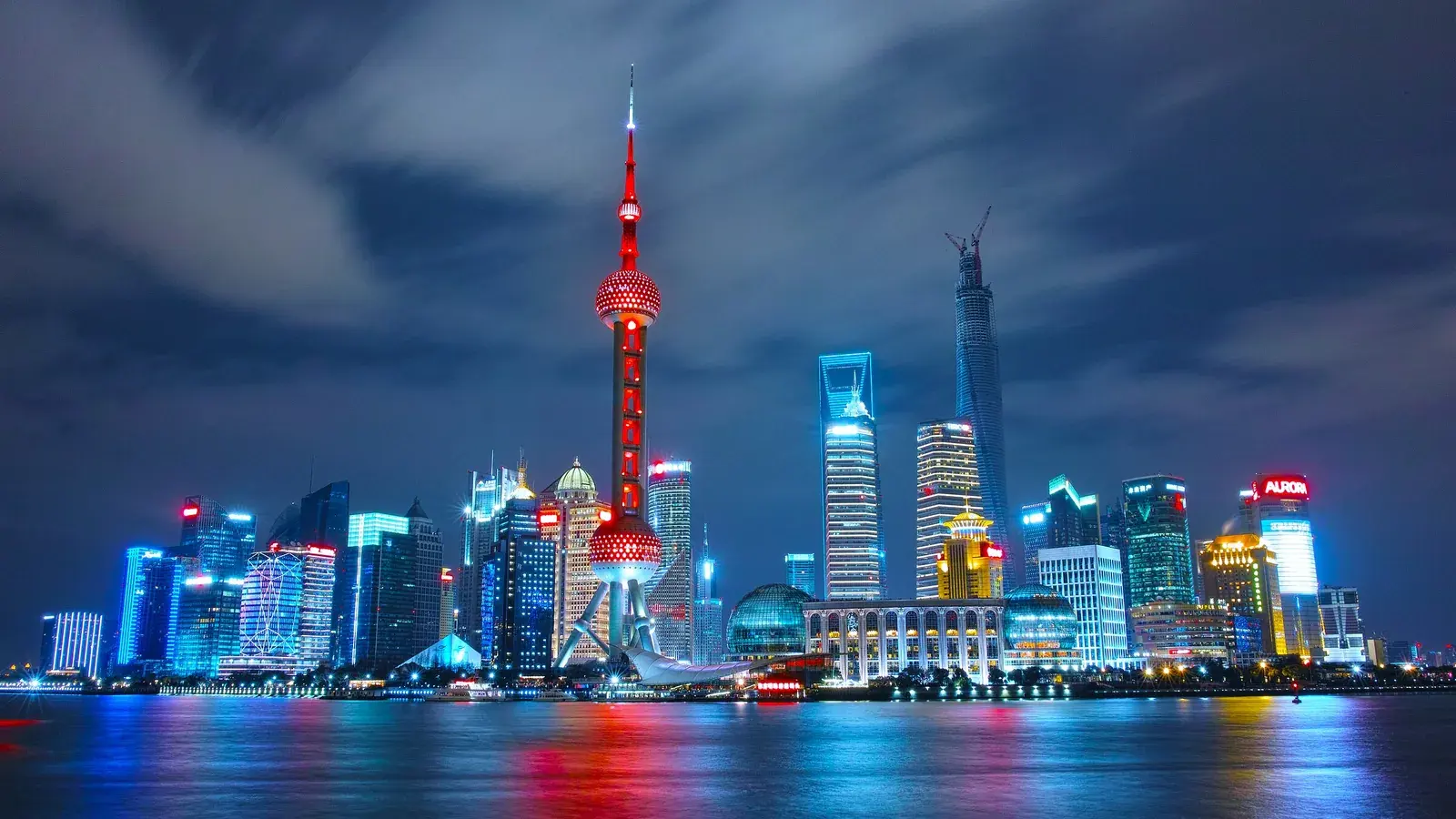 The Shanghai skyline at night from across the river, lit towers reflected in the water