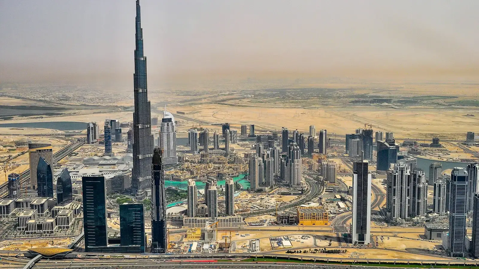 Dubai from the air, a tapering supertall tower above the downtown blocks with desert beyond