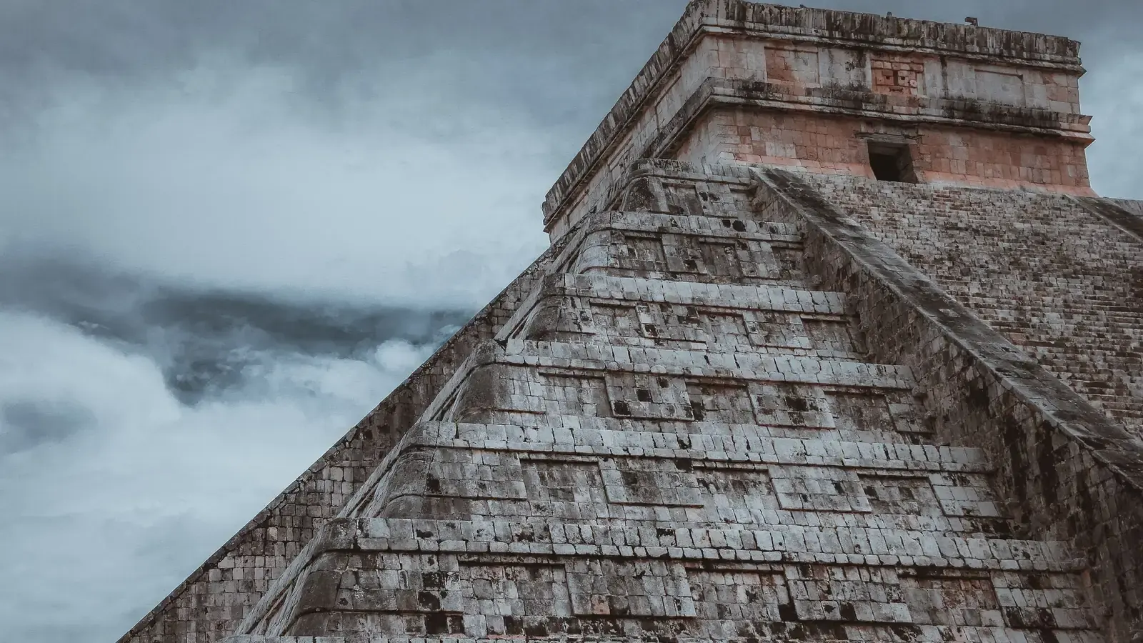 The stepped stone pyramid at Chichen Itza rising into heavy cloud