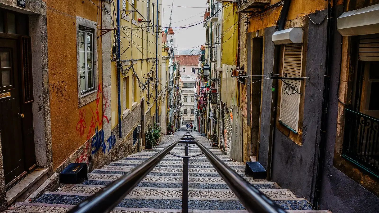Funicular rails running down a steep Lisbon street between ochre and yellow houses