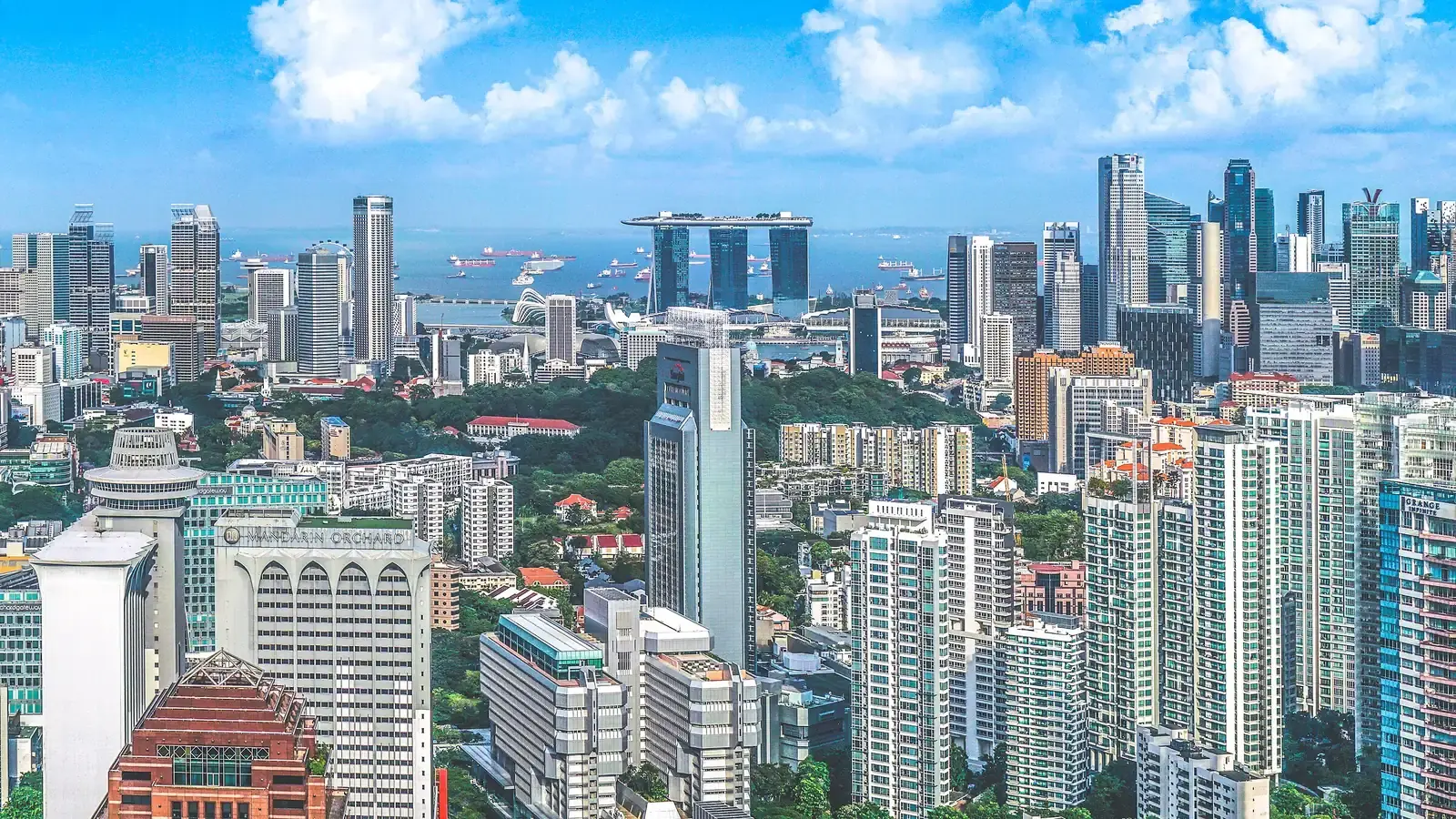 The Singapore skyline in daylight, a three-towered hotel on the bay and ships at anchor