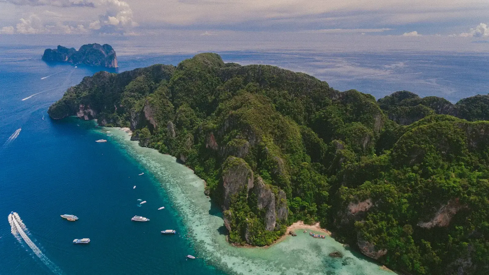 An aerial view of a forested limestone island, boats moored over turquoise reef