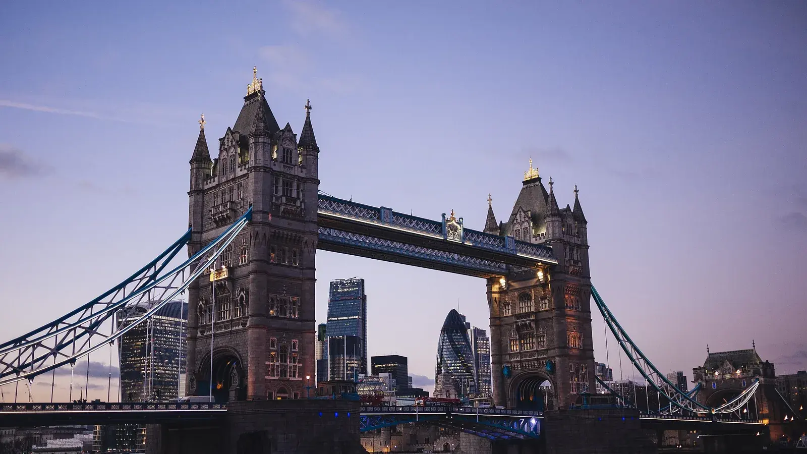 Tower Bridge lit at dusk, the towers of the City of London standing behind it
