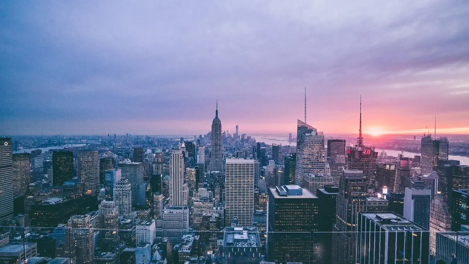The Manhattan skyline at dusk from a rooftop, a tall spired tower against a pink sky