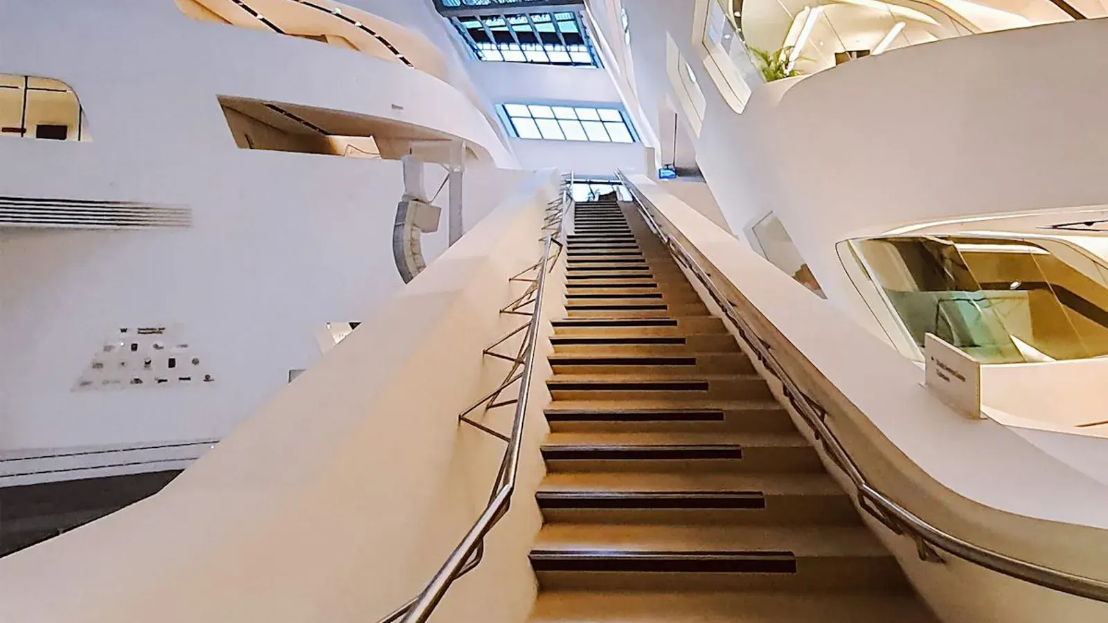 A pale curved staircase winding up through a bright modern atrium