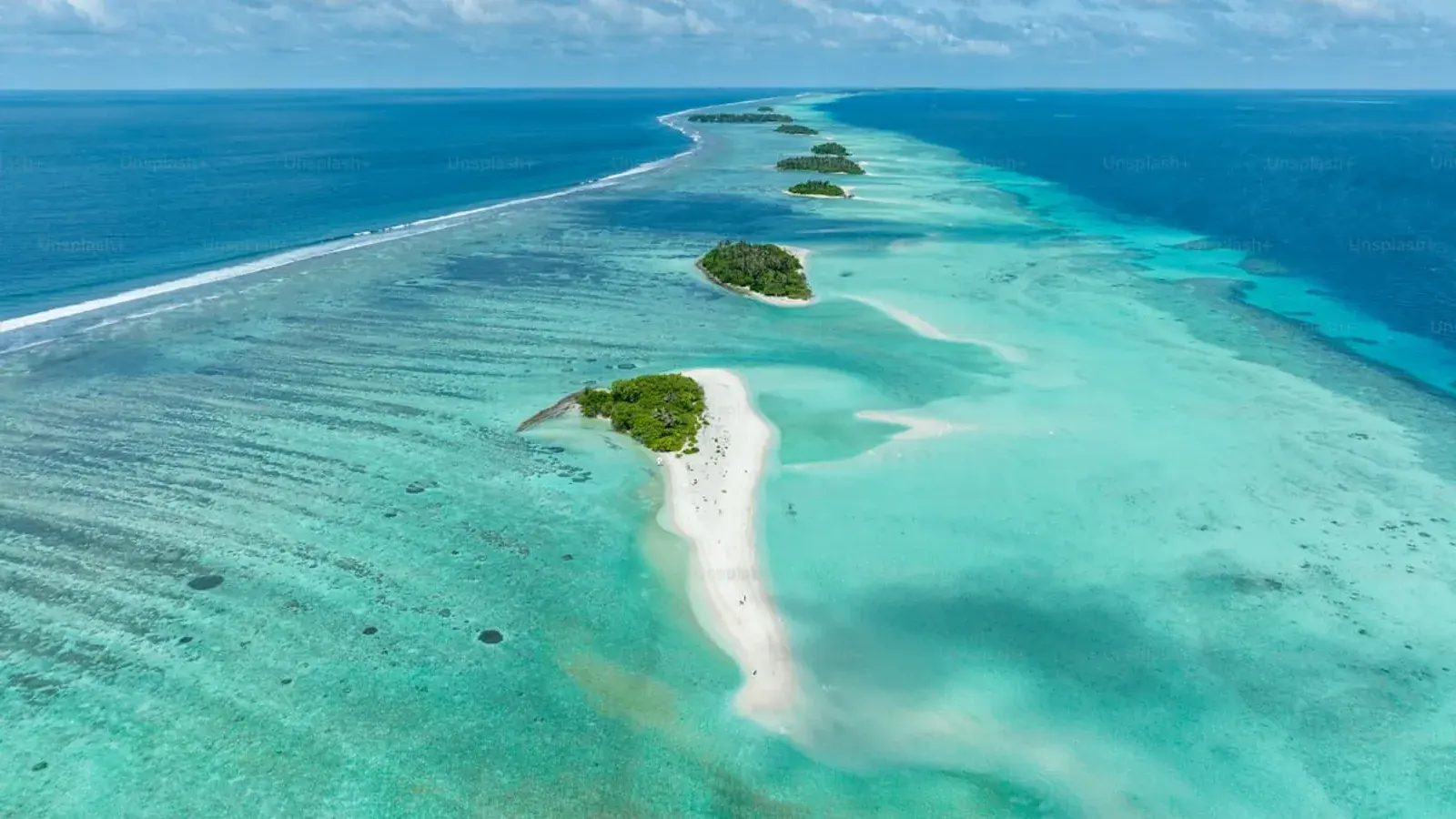 An aerial view of a chain of coral islets and sandbars in a turquoise sea
