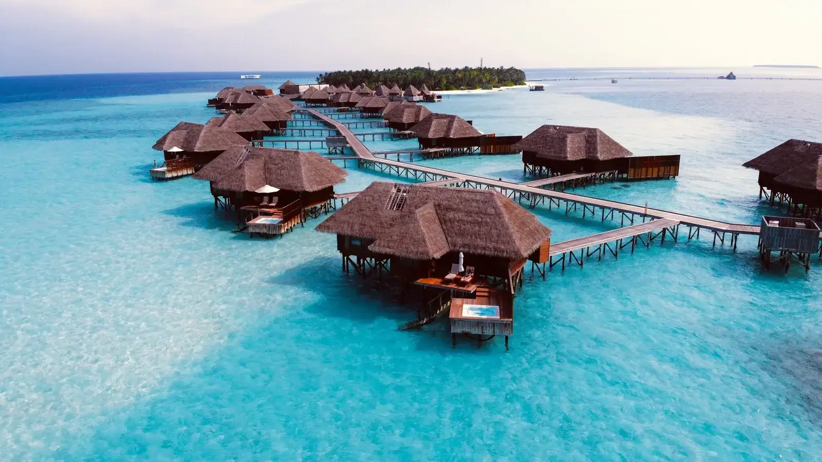 An aerial view of overwater villas curving away from a palm-covered island