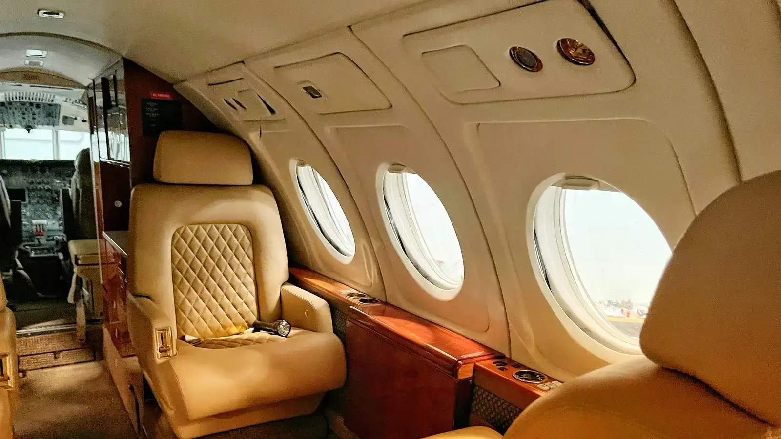 The cabin of a business jet, quilted cream seats between small oval windows