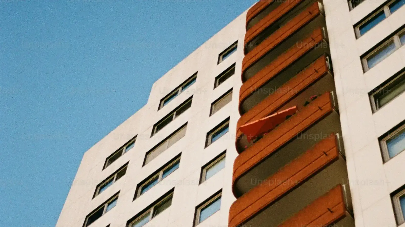 A pale apartment block with orange-shaded balconies against a clear sky