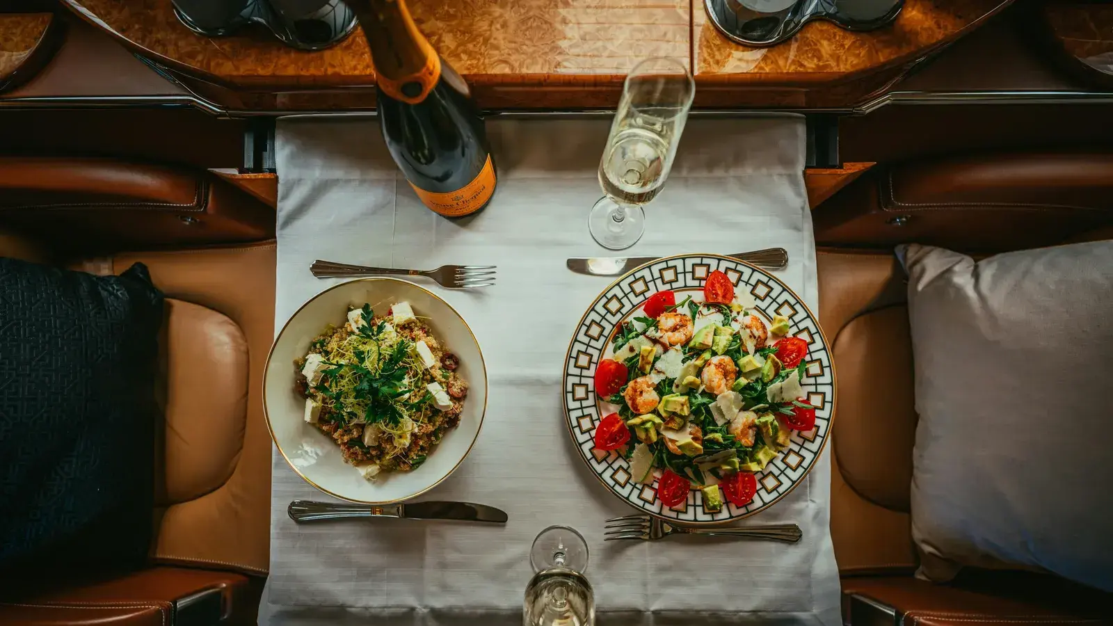 Two plated dishes and a bottle of champagne set out on a private jet's table