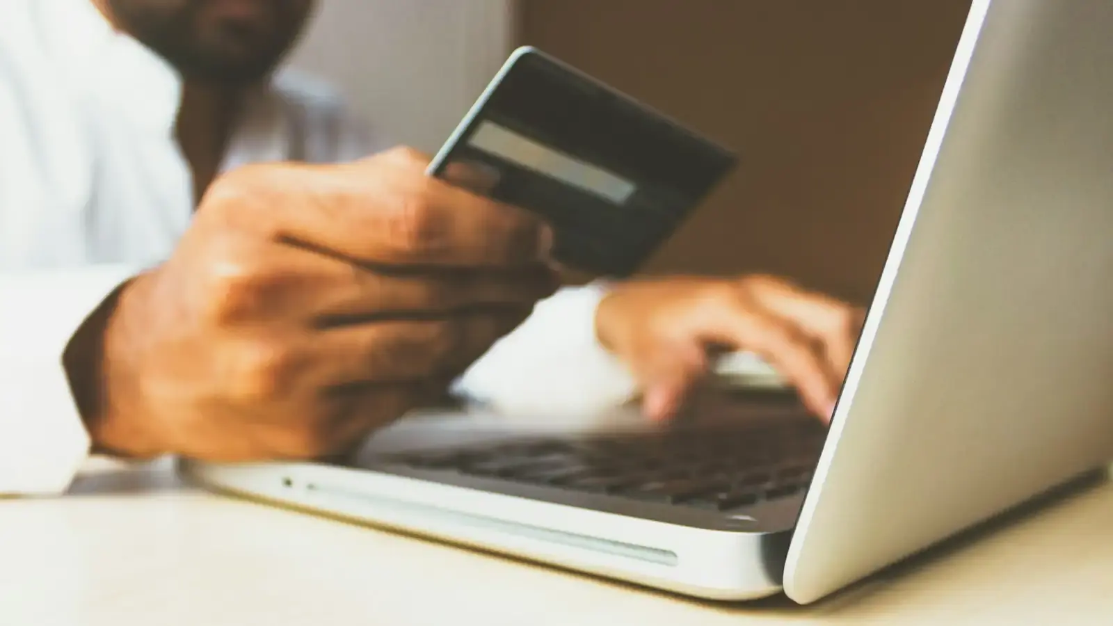A hand holding a bank card beside an open laptop, ready to type in card details