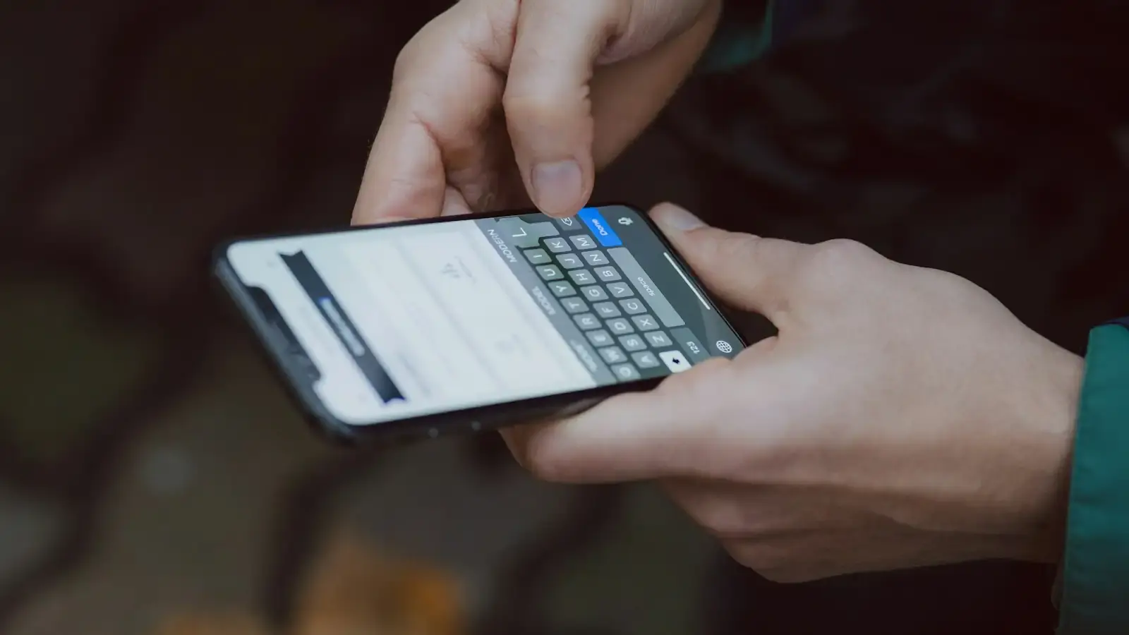 Two hands typing on a smartphone keyboard, a dark background behind