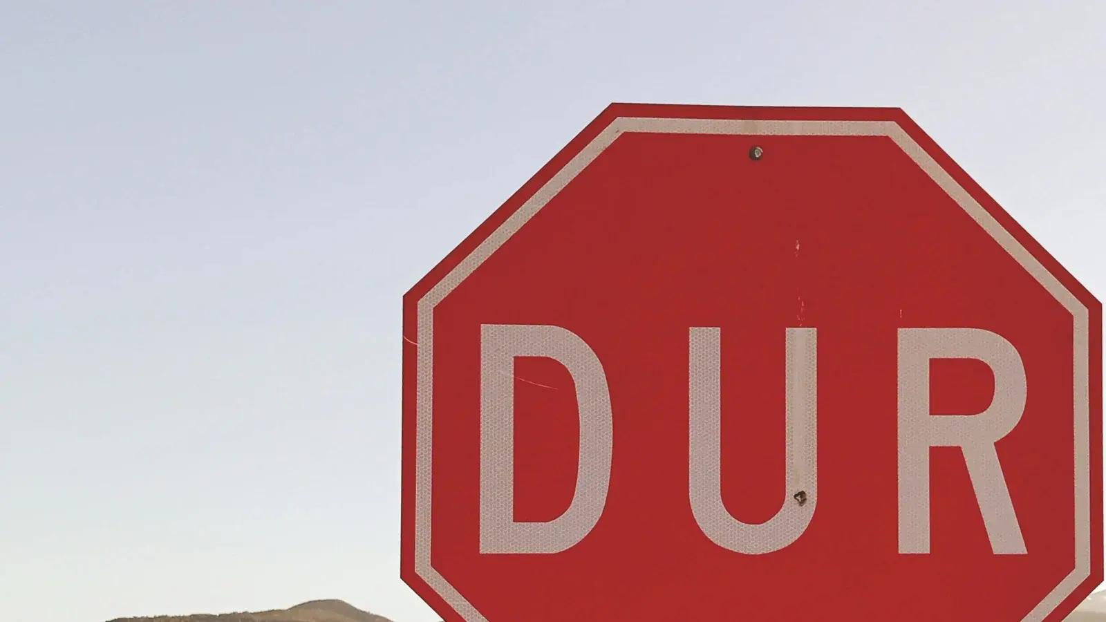 A red octagonal road sign reading DUR, the Turkish word for stop, against a pale sky