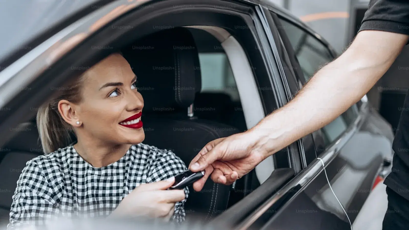 A woman in the driver's seat taking a set of car keys through the open window
