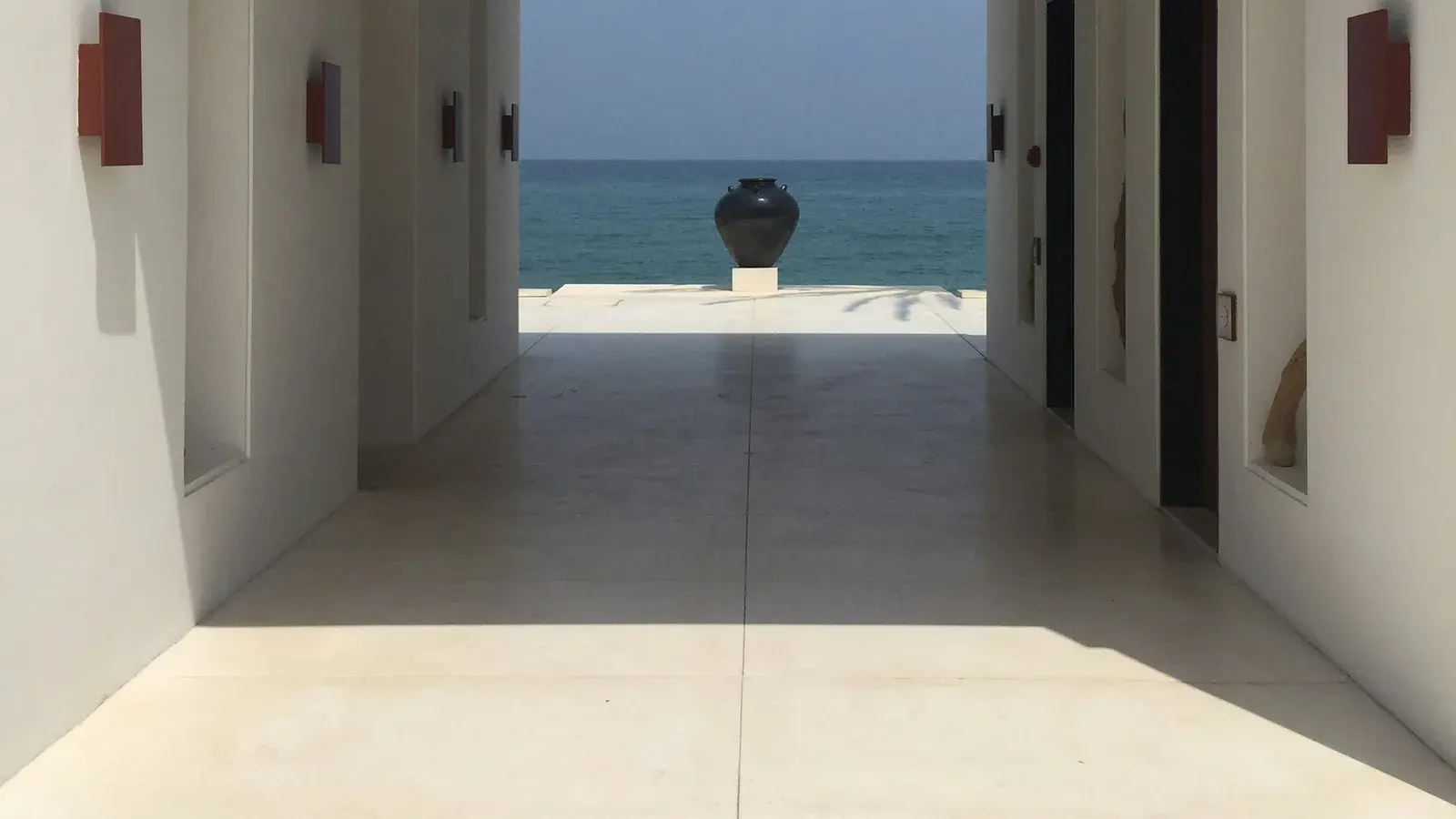 A whitewashed corridor opening onto the sea, a glazed jar on the step