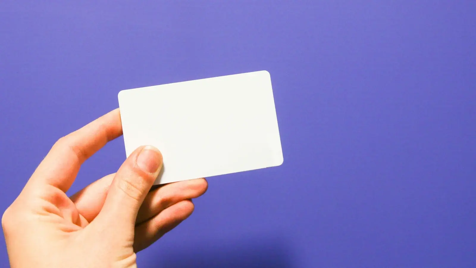 A hand holding a plain unbranded payment card against a violet background