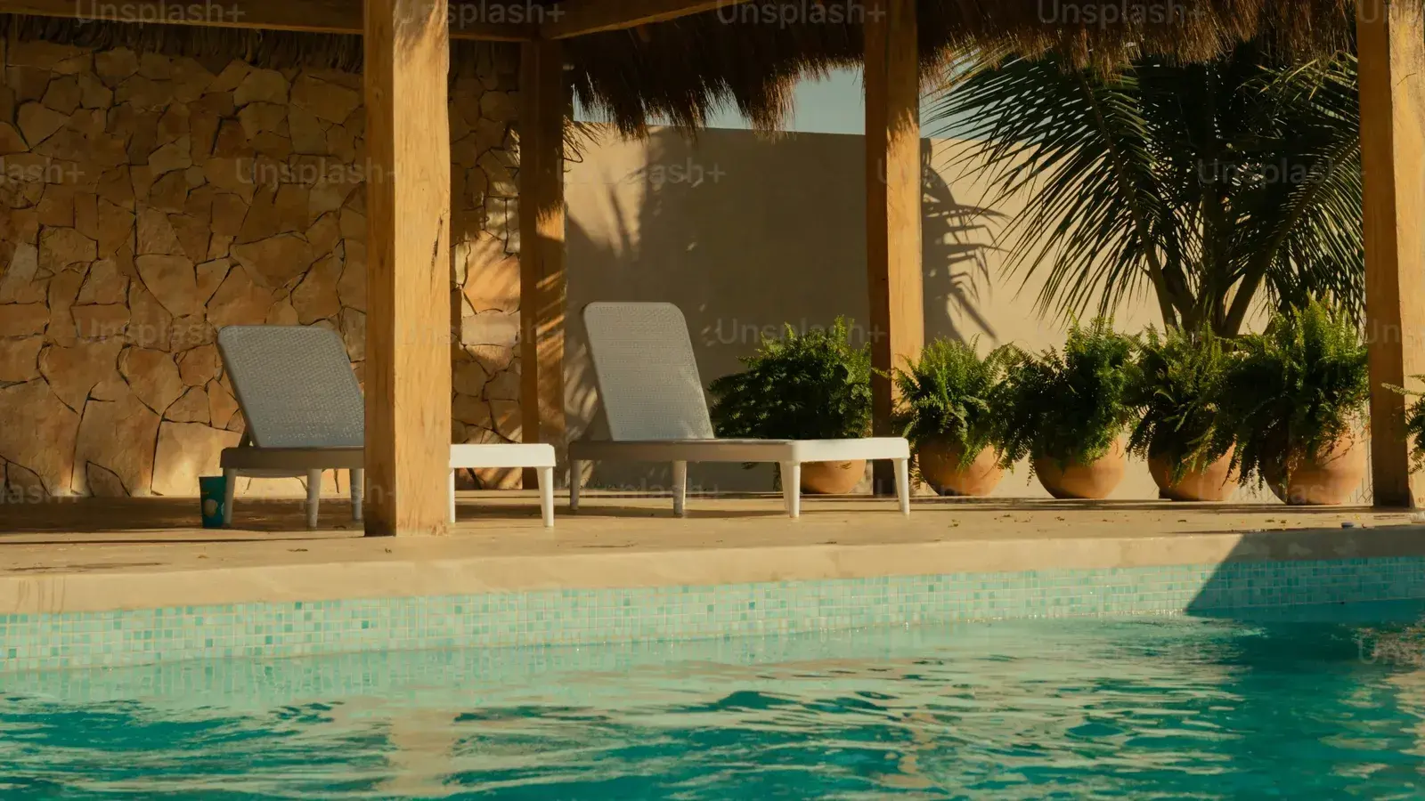 Two sun loungers under a palm-thatched shade beside a still pool