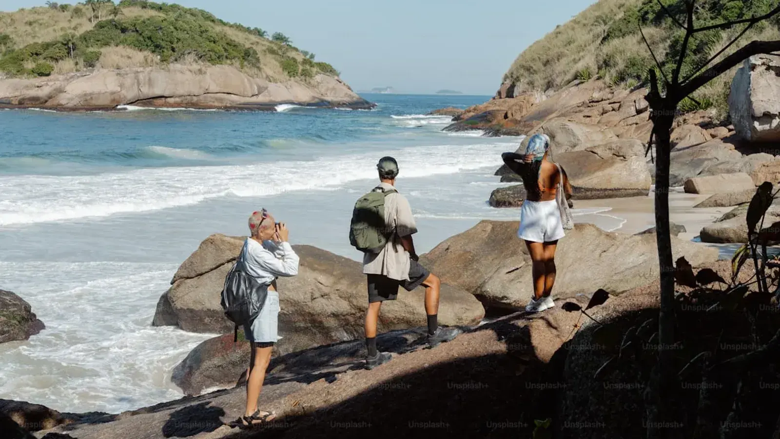Three people picking their way across coastal rocks above the surf