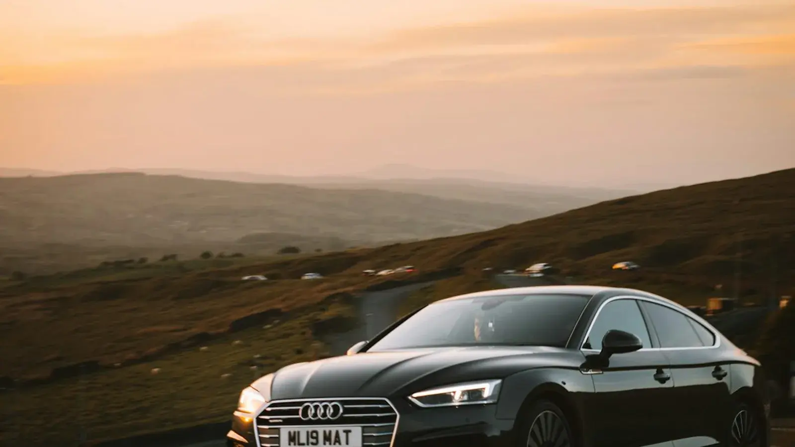 A black coupé parked on a moorland road at sunset