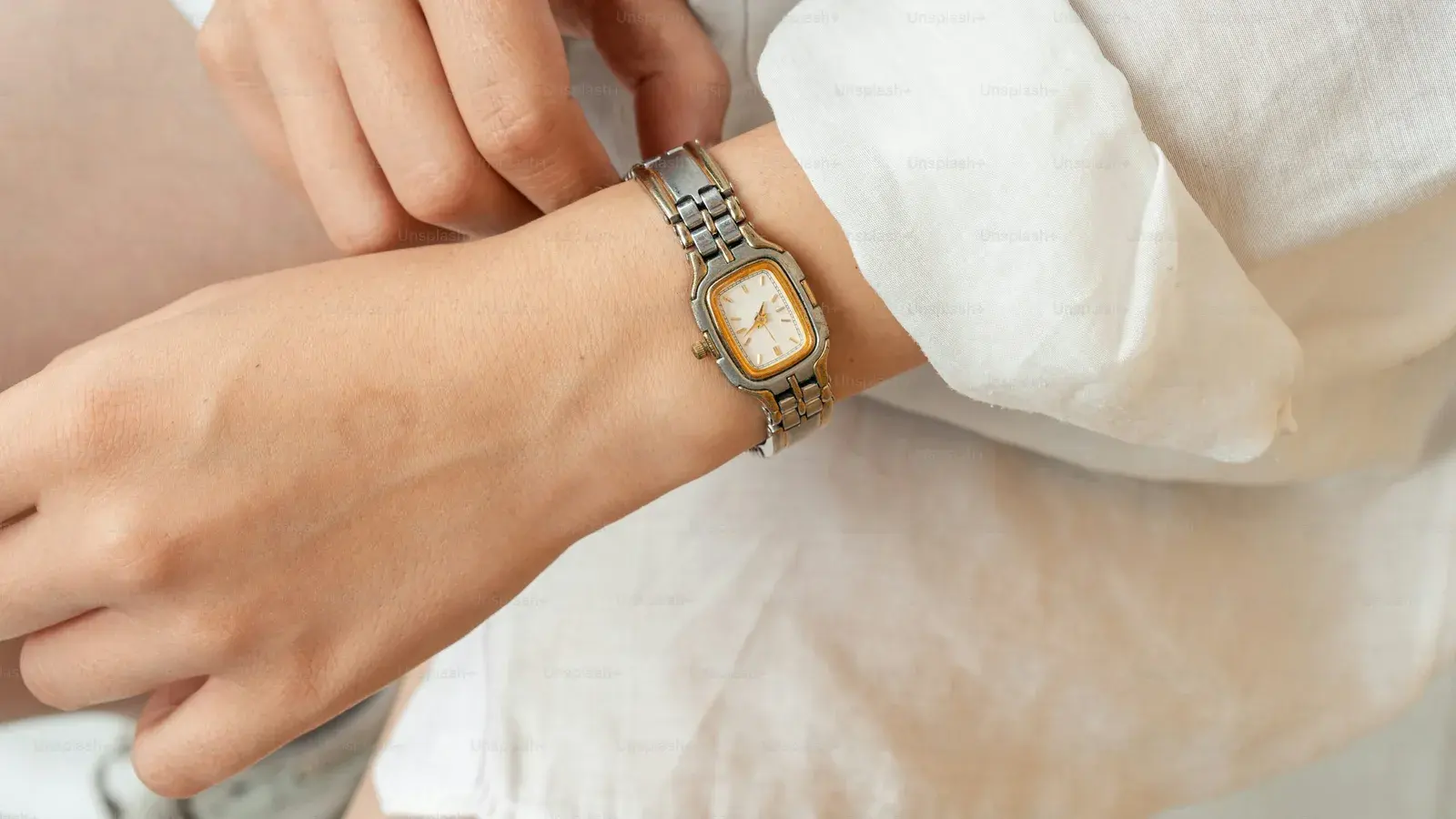 A slim two-tone dress watch with a white dial on a wrist