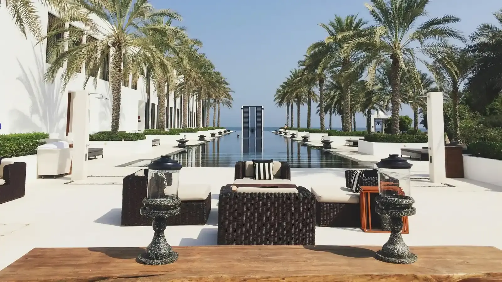 A white courtyard with a long reflecting pool and palms
