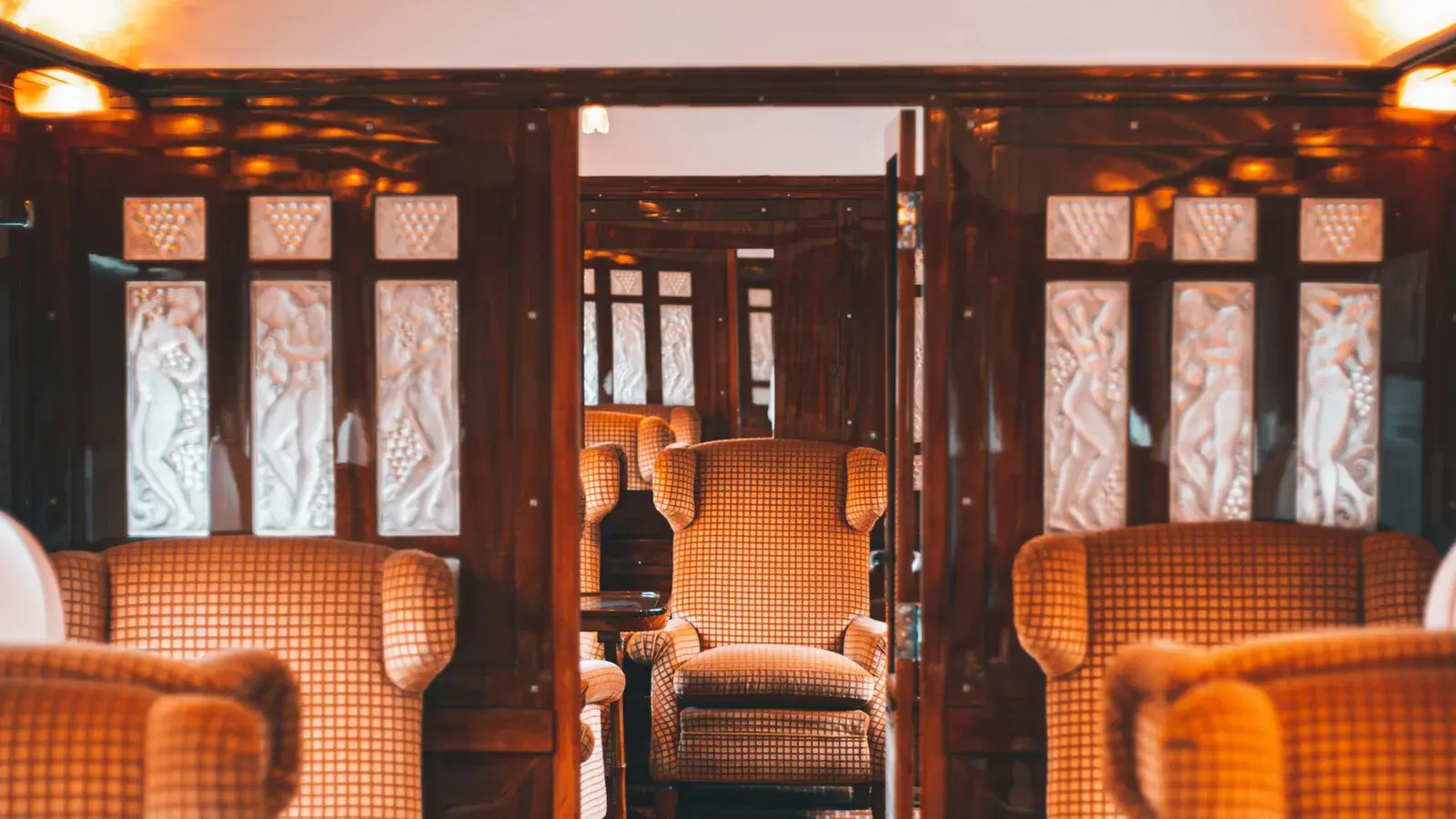 The panelled lounge car of a vintage train, armchairs beside etched glass