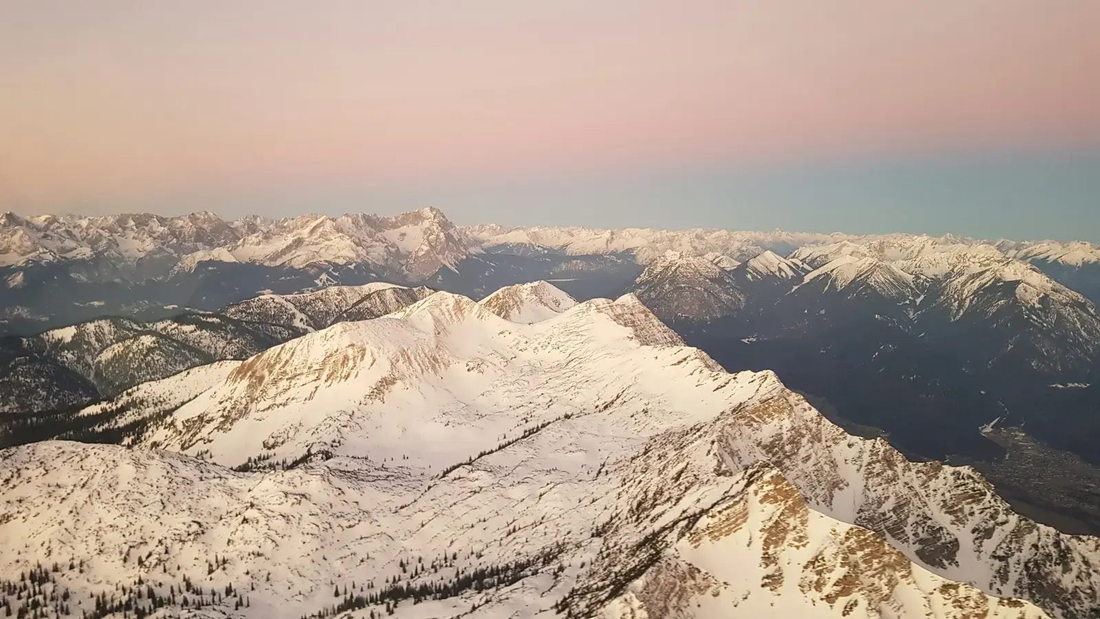 Snow-covered Alpine peaks seen from an aircraft at dusk, a pink sky above the ridges