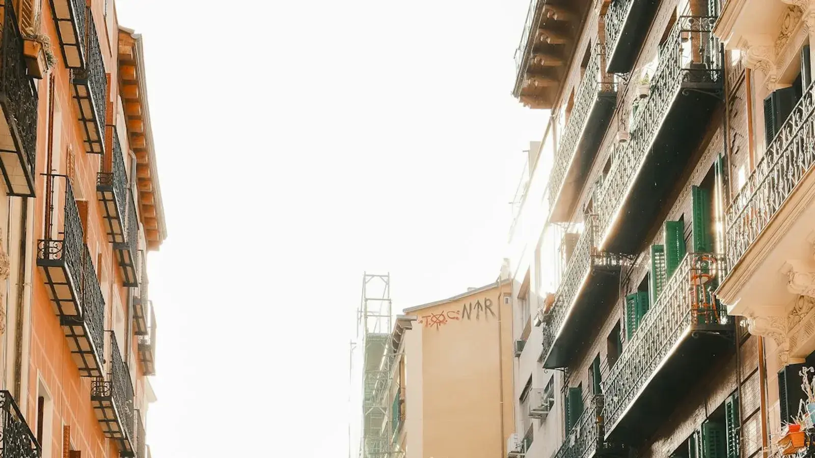 A sunlit street of apartment blocks with shallow balconies