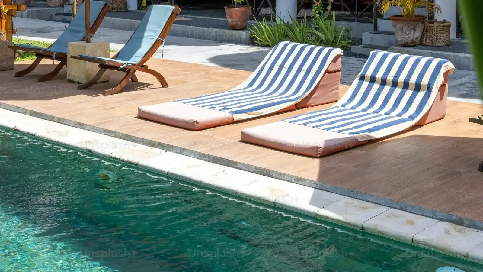 Two striped sun loungers on a tiled deck beside a pool