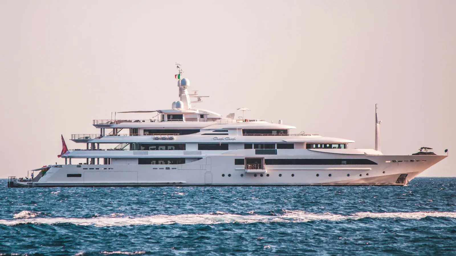 A large white motor yacht under way on open sea, an ensign at the masthead