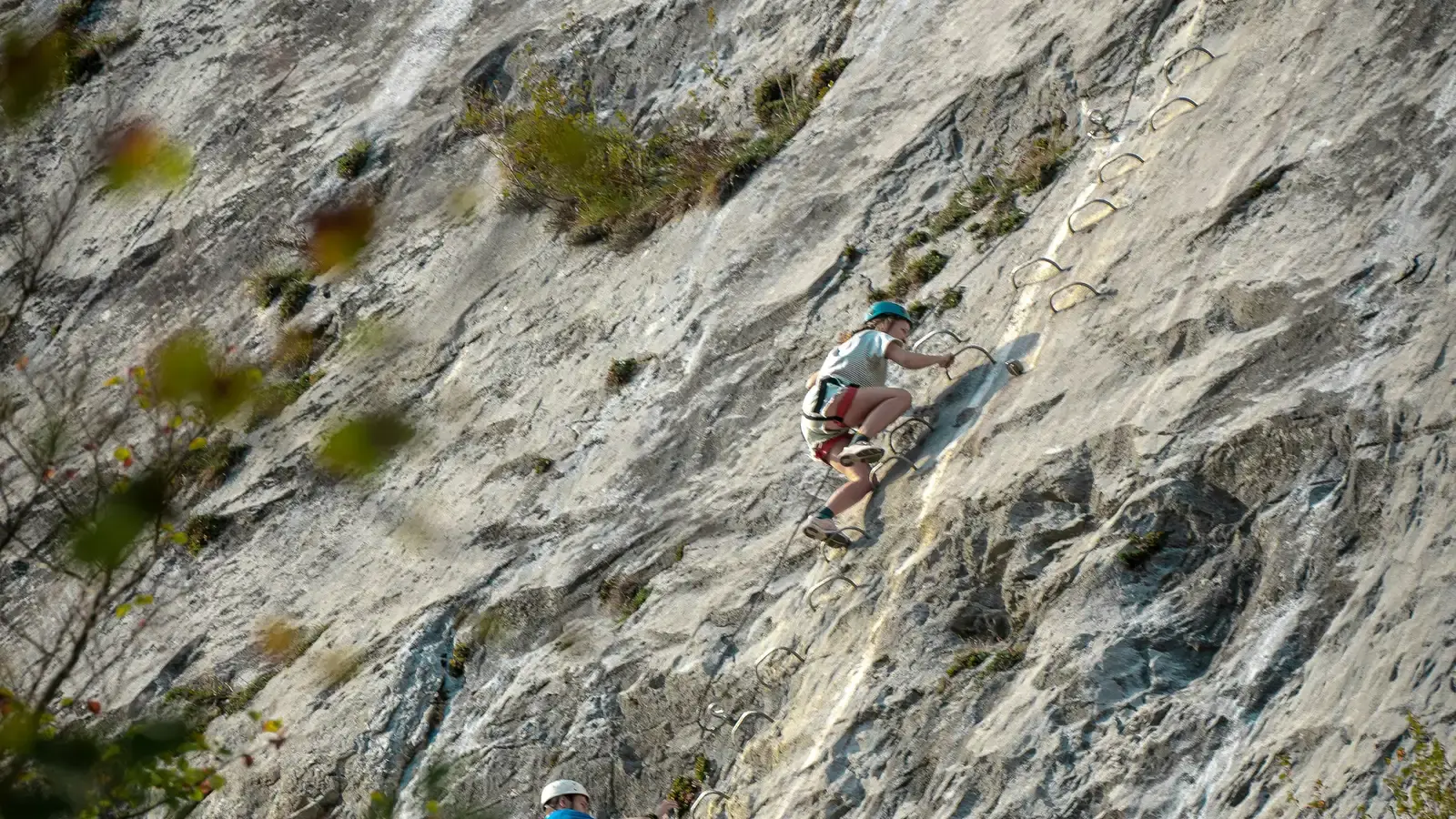 Two climbers on a via ferrata, iron rungs and a steel cable fixed across the rock face