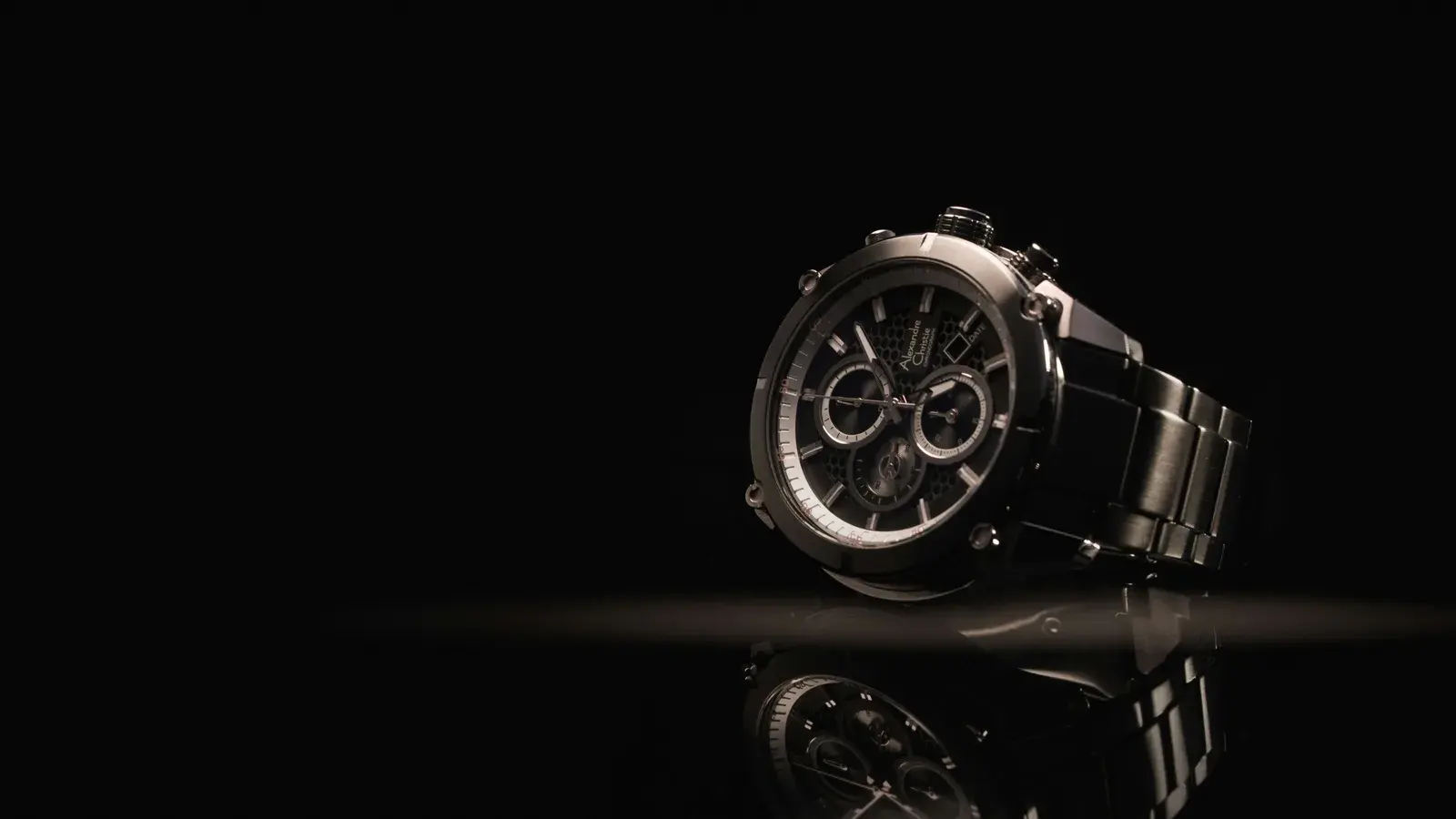 A steel chronograph lying on a black surface, subdials and tachymeter bezel
