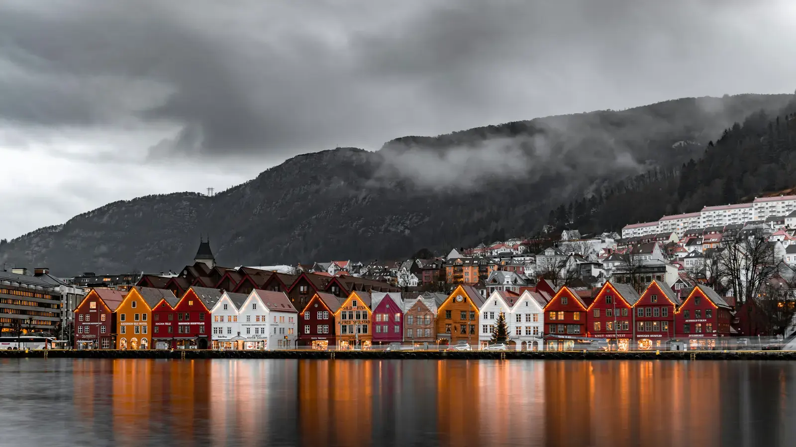 The lit wooden wharf houses of Bergen reflected in the harbour at dusk
