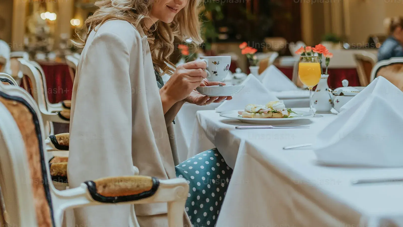 A woman lifting a teacup at a laid table in a grand hotel dining room