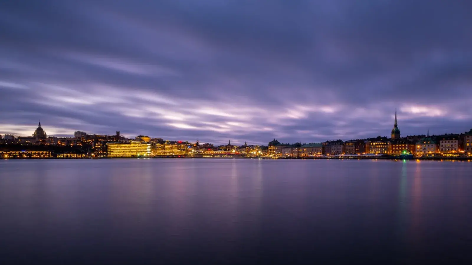 A city skyline at dusk across the water, spires above lit windows