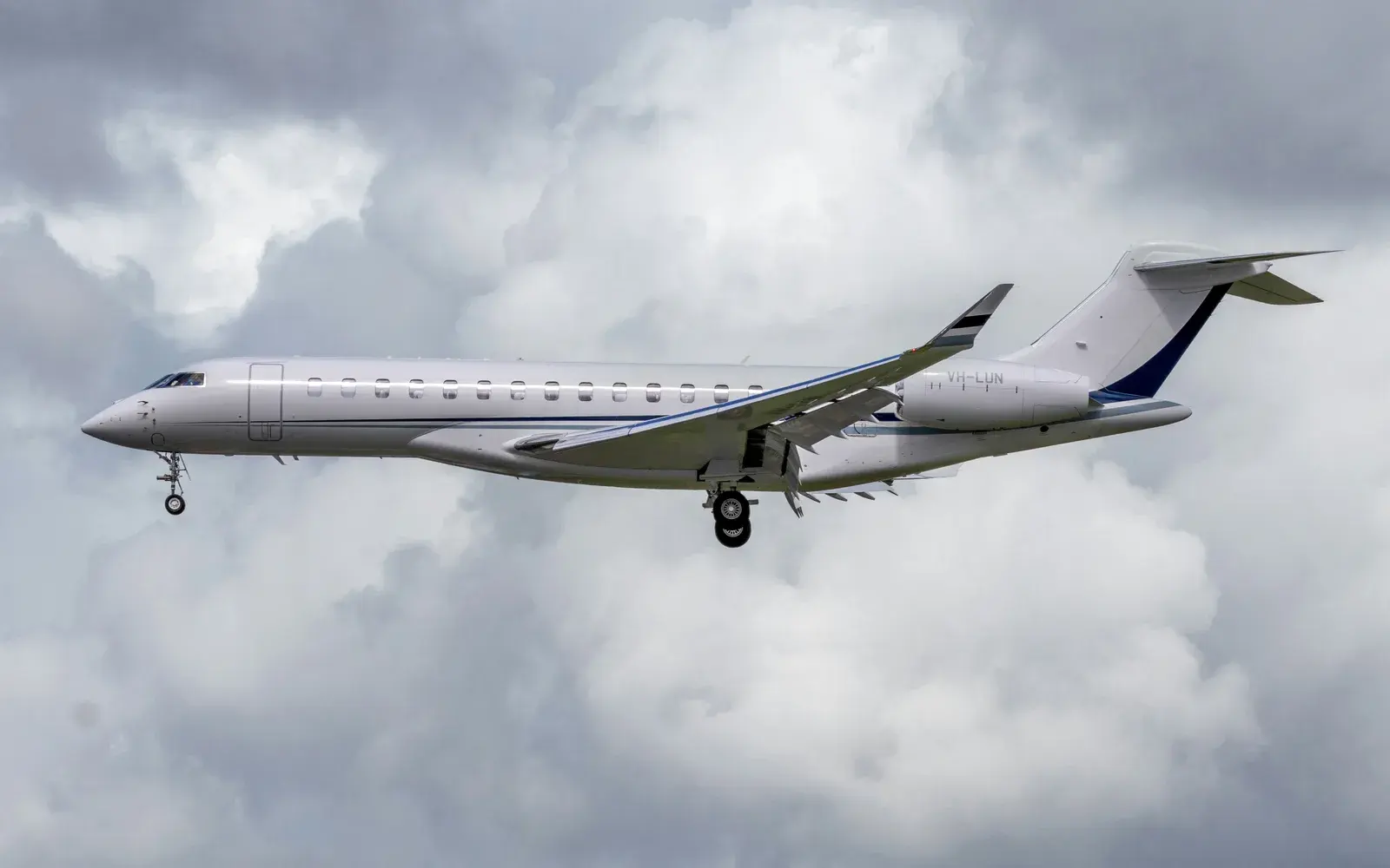 A long business jet on approach with its gear down against grey cloud