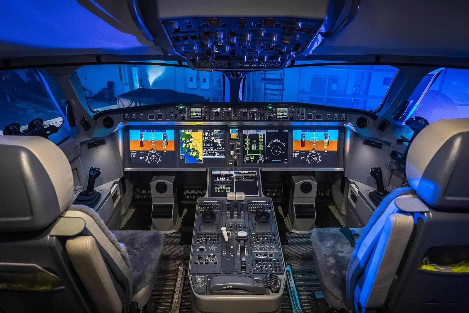 An airliner flight deck at night, six instrument screens lit against blue cabin light