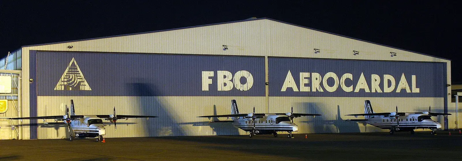 Twin-turboprops parked at night in front of a lit private aviation hangar
