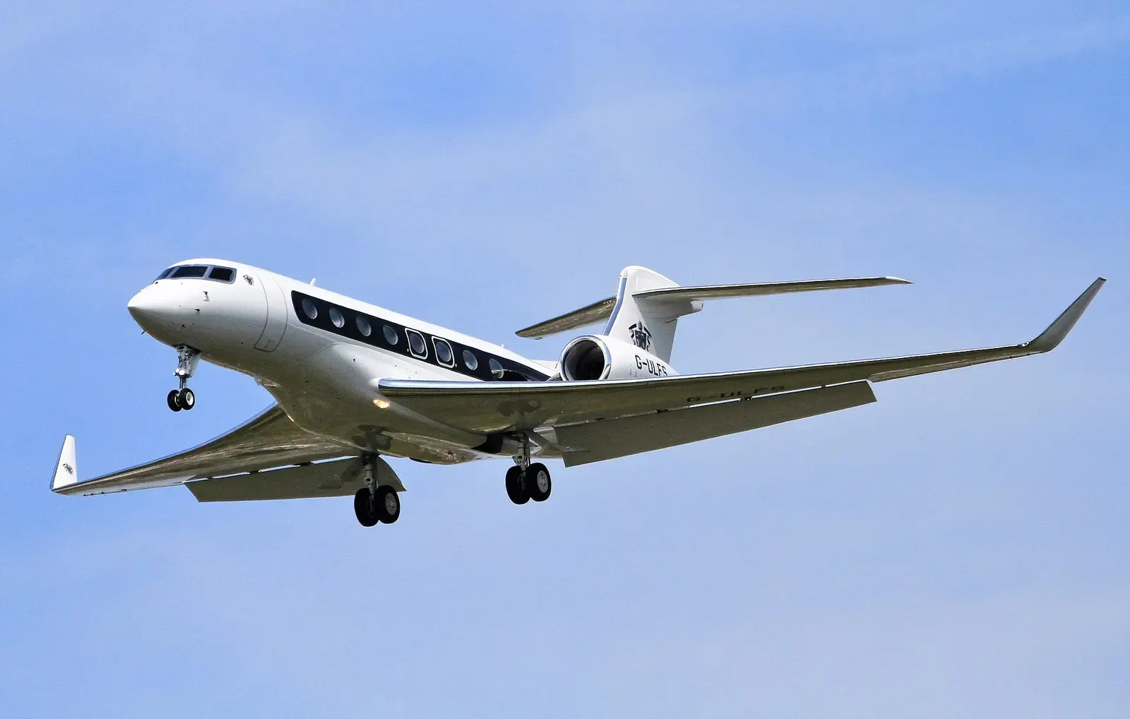 A long-range business jet on final approach against a clear blue sky