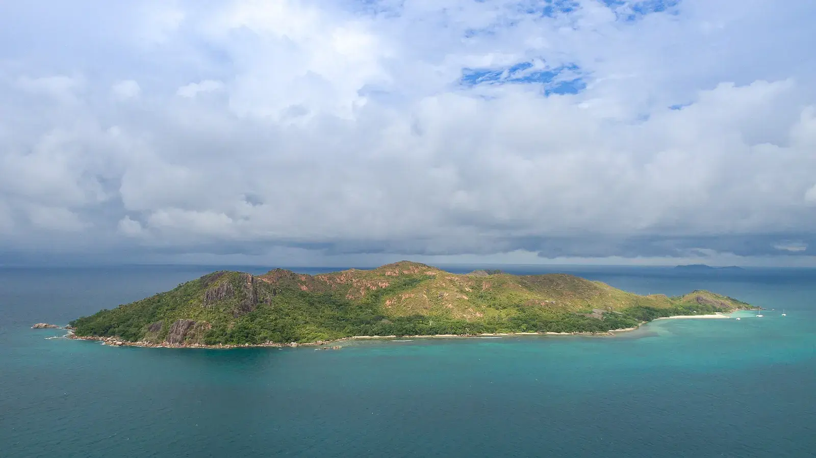 A green granite island seen across the sea under heavy cloud, two white boats off the beach at one end