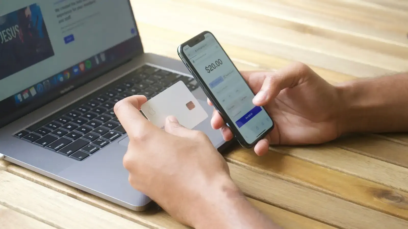 Hands holding a bank card over a laptop keyboard while a smartphone shows a payment amount