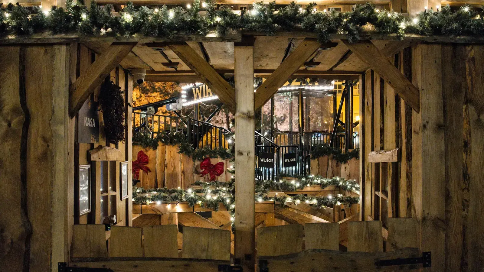 A wooden Christmas market stall at night, its beams hung with fir garlands and white fairy lights