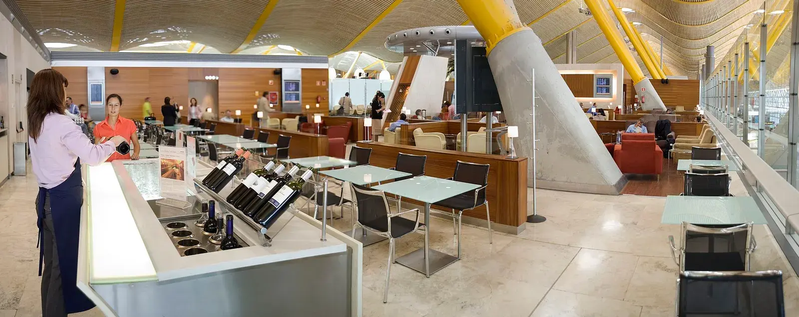 An airport lounge under a yellow-ribbed roof, a wine bar in the foreground
