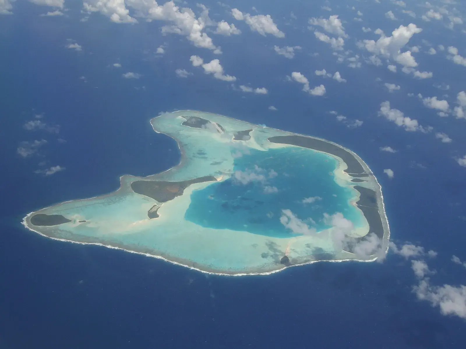 An aerial view of a whole coral atoll, a pale lagoon ringed by dark reef in deep blue ocean