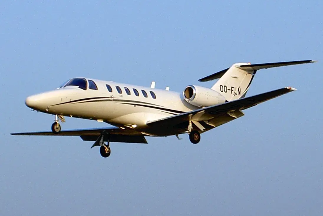 A light business jet on approach, gear down against a clear sky